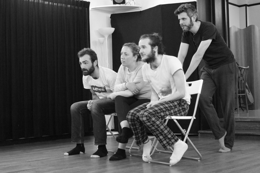 Photo en noir et blanc d'un atelier d'impro, des élèves sont assis, le coach est debout derrière elleux